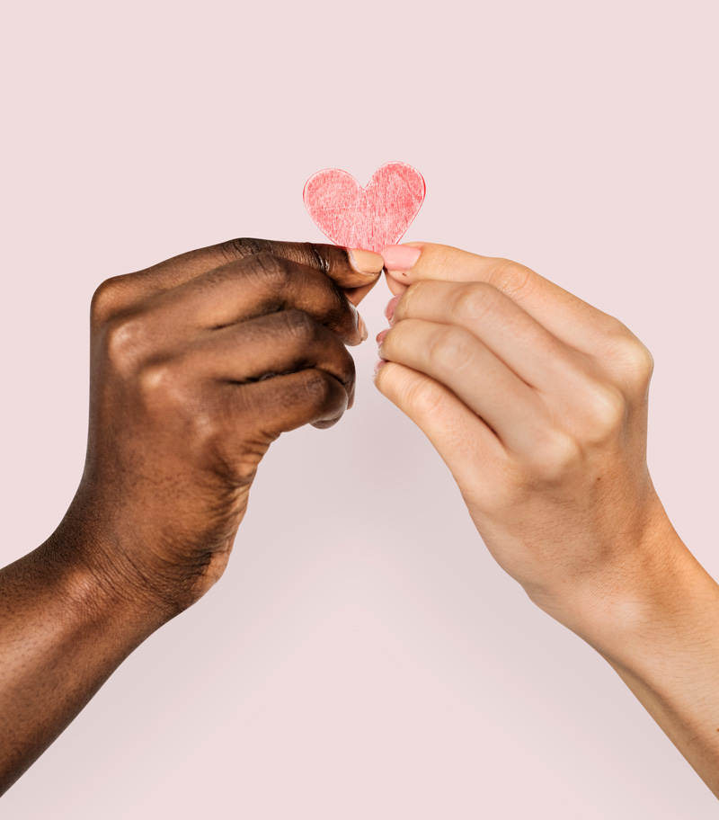 Bi-racial hands holding a paper heart together